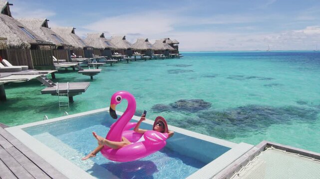 Pool Beach Vacation travel woman on inflatable Flamingo float mattress using phone in swimming pool. Girl sunbathing enjoying holidays resort. Raw unedited video of real woman model without makeup