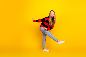 Cheerful young woman posing playfully in a trendy striped sweater against a vibrant yellow...