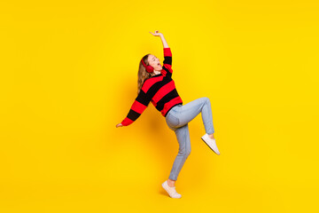 Naklejka premium Cheerful young woman in a striped sweater posing energetically against a bright yellow background showcasing stylish casual fashion.