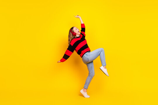 Cheerful young woman in a striped sweater posing energetically against a bright yellow background showcasing stylish casual fashion.