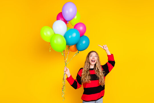 Cheerful young woman with vibrant balloons wearing striped sweater posing against a yellow background