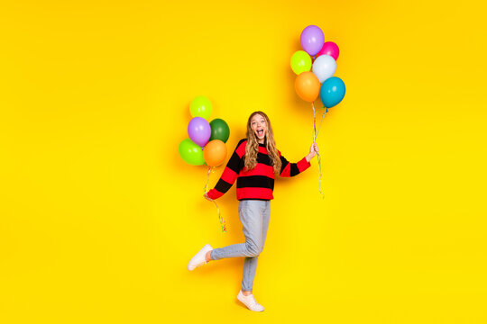 Cheerful girl in casual striped sweater holding colorful balloons against bright yellow background, spreading joyful vibes