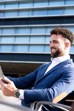 Businessman using digital tablet while sitting outside modern office building