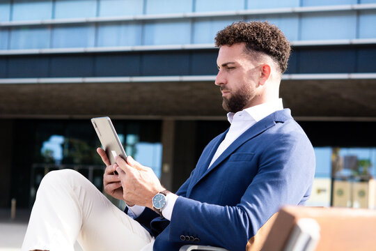 Businessman using digital tablet while sitting outside modern office building