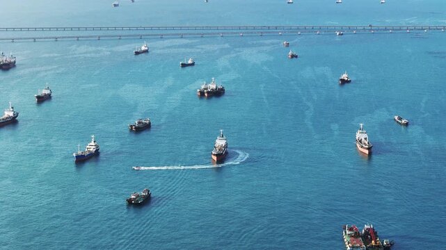 Fast patrol boat leaving a white wake while speeding past an oil tanker ship and anchored cargo vessels in the blue sea. Maritime logistics, port security, and offshore energy transport concept.
