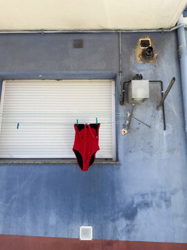 Colorful urban scene reflecting the distinctive atmosphere of everyday life in Spain, with a red swimsuit hanging on a clothesline against a weathered blue facade.