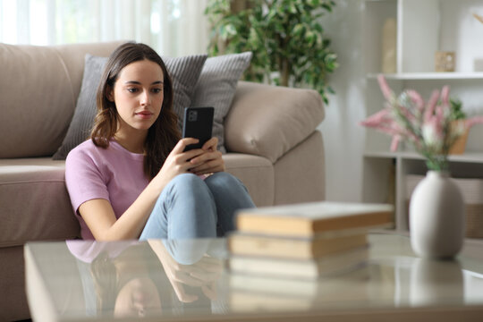 Serious woman checking smartphone in the living room