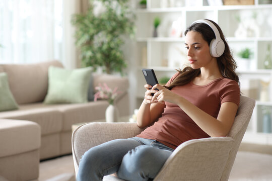 Serious woman wearing headphone checking playlist on phone