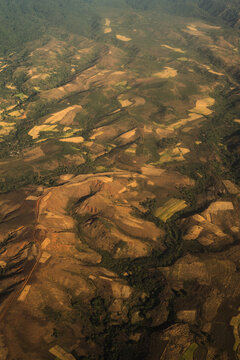 Aerial view of the rugged hilly landscape of Madagascar, featuring patchwork agricultural fields, patches of native forest, and winding dirt roads under the warm light of the golden hour.