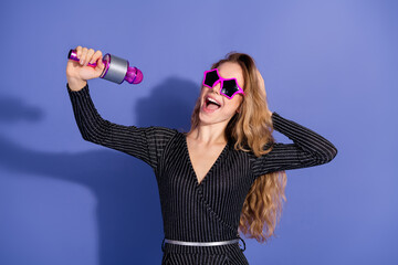 Young woman singer with pink star sunglass singing into a shiny microphone in a striped jumpsuit...
