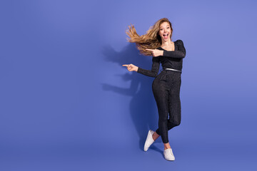 Young woman in striped jumpsuit leaps in a studio with purple background and playful smile