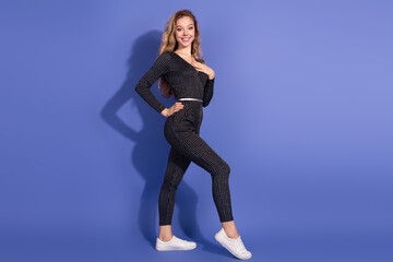 Young stylish woman in striped jumpsuit poses against blue background for fashion and lifestyle...