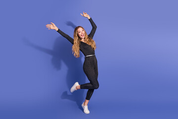Naklejka premium Young woman in striped jumpsuit leaps with joy against blue background showcasing playful fashion and lifestyle moment