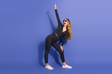 Young woman in striped jumpsuit points up smiling against blue background for lifestyle fashion and...