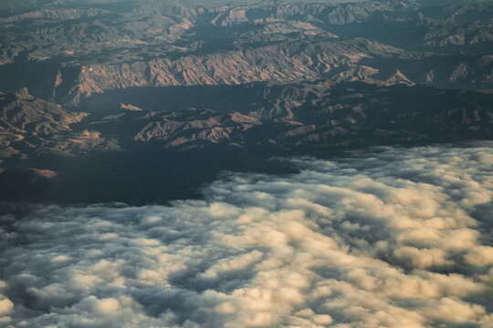Aerial view of rugged mountain ranges partially covered by a thick layer of low-hanging clouds under soft morning light, Madagascar.