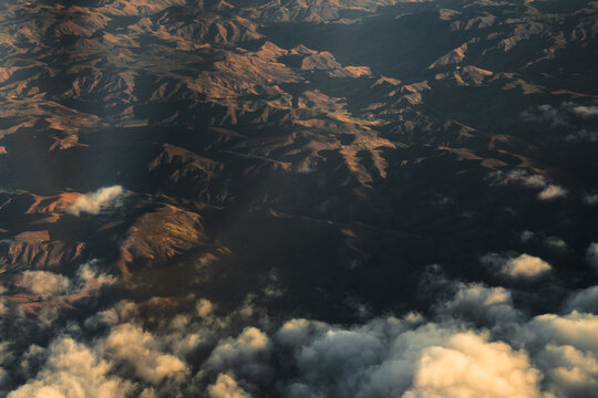 Aerial view of rugged mountainous landscape in Madagascar during golden hour with scattered clouds casting shadows over the terrain.
