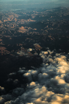 Aerial view of the rugged mountainous landscape featuring deep valleys, dramatic shadows, and a thick layer of clouds illuminated by the golden hour light, Madagascar.