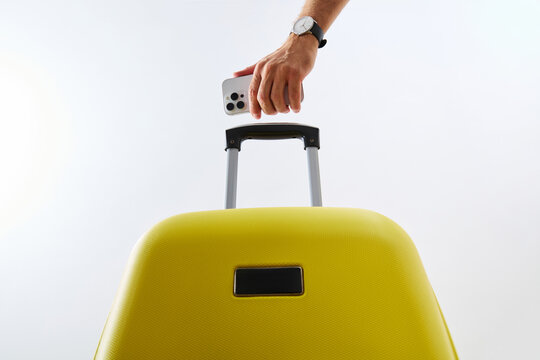 Hand Holding Smartphone Over Yellow Suitcase Isolated on White Background