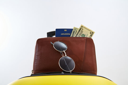 Travel Essentials with Passport, US Dollar Bills, Sunglasses and Leather Bag on Yellow Suitcase
