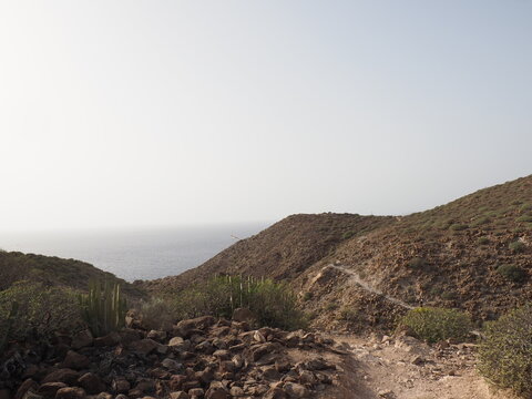 Narrow dirt path leading through a rocky mountain pass towards the sea
