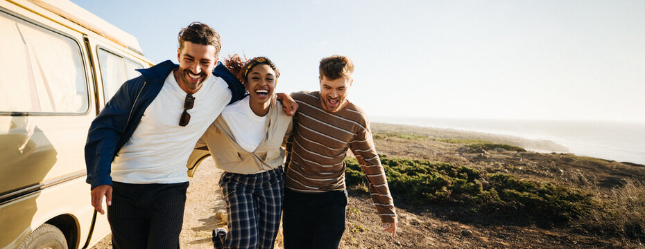 Friends on road trip laugh together by vintage van along coastal trail