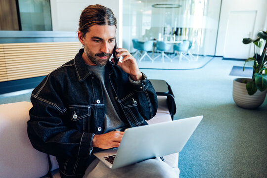Man on laptop talks on phone in office
