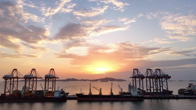 Silhouettes of gantry cranes and cargo ships at a bustling seaport during a dramatic golden sunset. Global maritime logistics, international trade, and industrial shipping transport concept.
