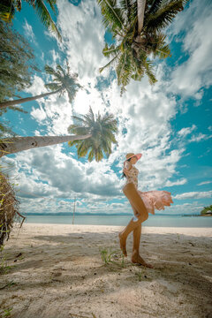 Woman tourist stay under shadow of the coconut trees at the edge of the sea beach, cheerfully traveling life in summer of the island