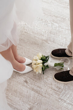 Overhead view of bride and groom shoes with a white rose bouquet on a wooden floor