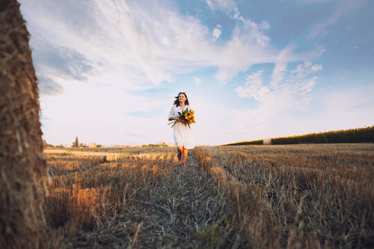 woman in a white dress holding a bouquet of wild flowers with sunflowers in a field
