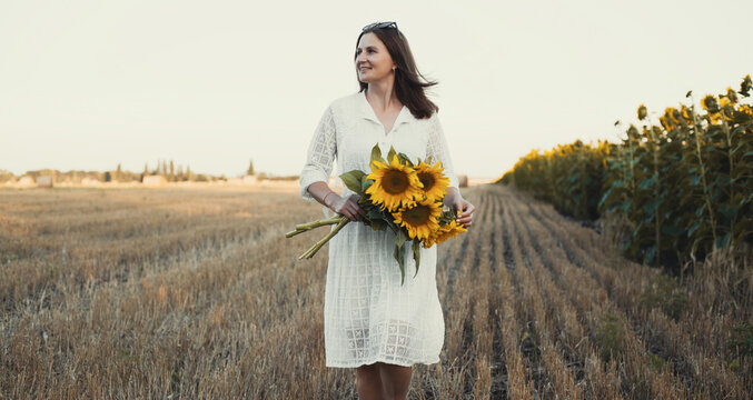 woman in a white dress holding a bouquet of wild flowers with sunflowers in a field