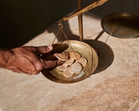 Gold coins in a brass beam balance pan, featuring a textured hand and warm amber glow for investment and wealth concepts with copy space