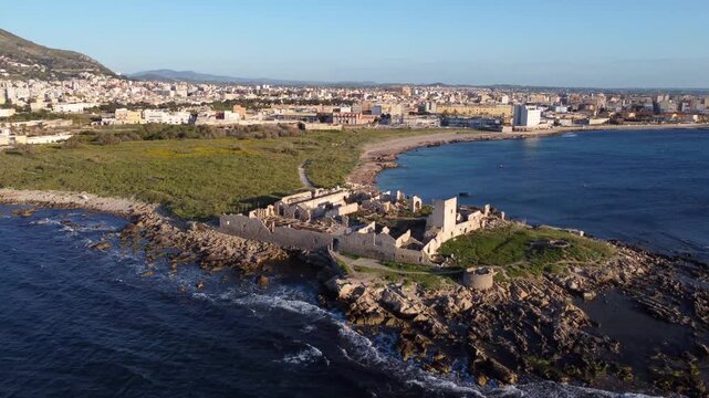 Aerial view of ancient ruins on rocky coastline overlooking Trapani city at sunset.