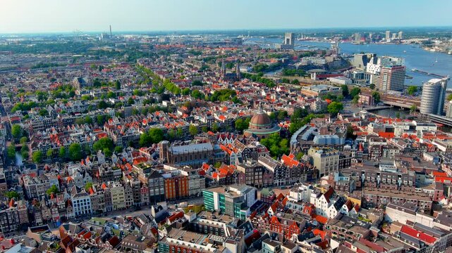 Aerial drone view over the rooftops of the Amsterdam historic center with the Koepelkerk dome, Nieuwe Kerk, canal houses, the IJ river and the western harbor, Netherlands, in summer.