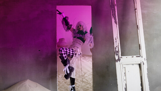 Dancer in harlequin tights raising leg high in magenta lit doorway of derelict room