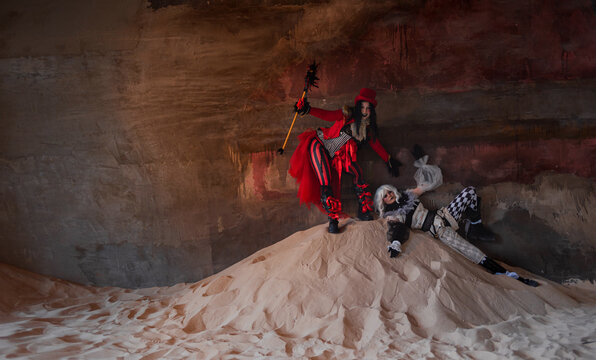 Two costumed performers on a sand dune inside vast dark abandoned industrial hall