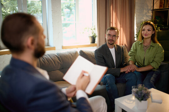 Family psychologist taking notes while listening to couple during therapy. Concept of clinical notes, attentive listening, relationship assessment.