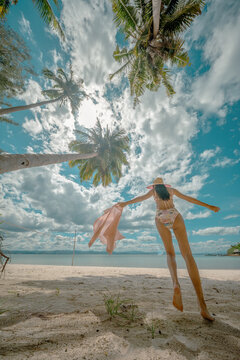 Woman tourist stay under shadow of the coconut trees at the edge of the sea beach, cheerfully traveling life in summer of the island