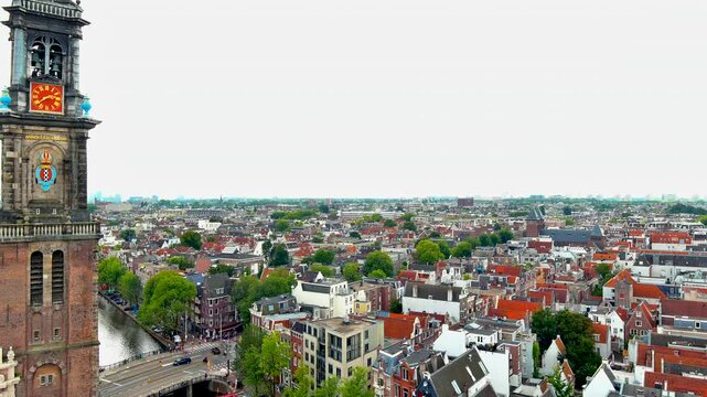 Aerial drone close-up of the Westertoren, the clock tower of Westerkerk church in Amsterdam, with bells, city coat of arms, clock face and Jordaan district rooftops, Netherlands.
