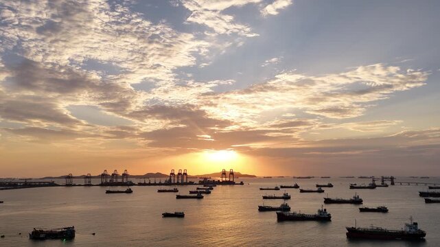 Silhouettes of gantry cranes and cargo ships at a bustling seaport during a dramatic golden sunset. Global maritime logistics, international trade, and industrial shipping transport concept.