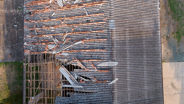 Aerial view of a damaged rural house roof with missing terracotta tiles and exposed wooden rafters after a storm, showing structural damage in Castelvetro Piacentino, Emilia-Romagna, Italy.