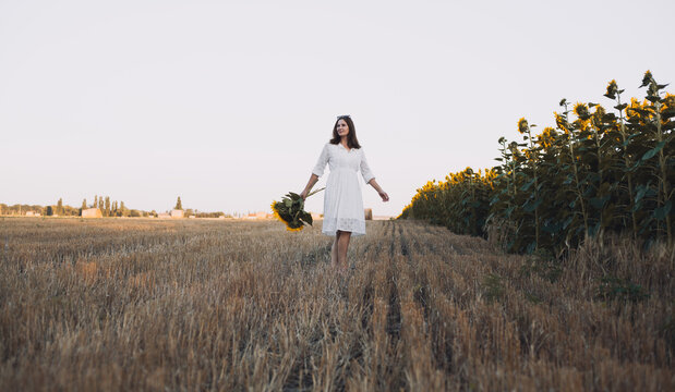 woman in a white dress holding a bouquet of wild flowers with sunflowers in a field