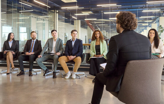 Coach giving presentation to coworkers at meeting. Business people attend a corporate workshop in an office, taking notes and discussing strategy with the trainer. Core concept is team learning.