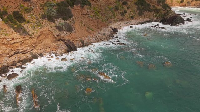Pebbles And Rugged Coastal Cliffs Line The Mediterranean Shoreline Near Masua In The Sulcis-Iglesiente, Sardinia, Italy. Aerial Shot