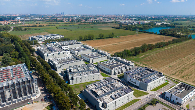 Aerial view of DATA4 MILAN CAMPUS, a large data center complex with industrial buildings and rooftop cooling units, surrounded by fields and trees in Zona Industriale, Lombardia, Italy.