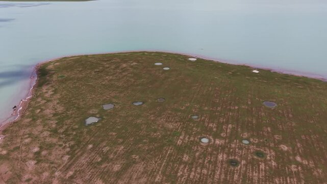 Drone rising and tilting up from a grassy spit dotted with pools to reveal the full width of Dau Tieng Reservoir with Ba Den Mountain beyond, Tay Ninh, Vietnam.