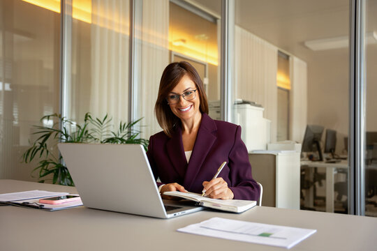 Cheerful businesswoman writing notes, using pen at office desk. 35 years old business woman works as executive manager leader, checking financial report, compiling annual statement. Copy space.