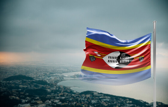 Eswatini flag waving over a coastal city under dramatic cloudy sky, realistic fabric motion, aerial seaside landscape background. Eswatini national flag for independence day.