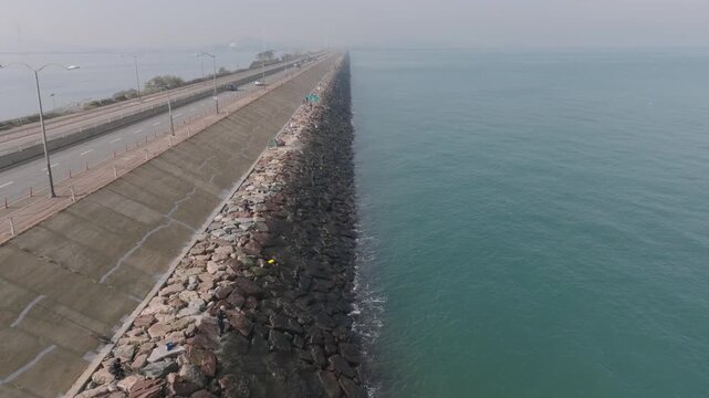 Aerial view of coastal road with breakwater and people fishing along shoreline.