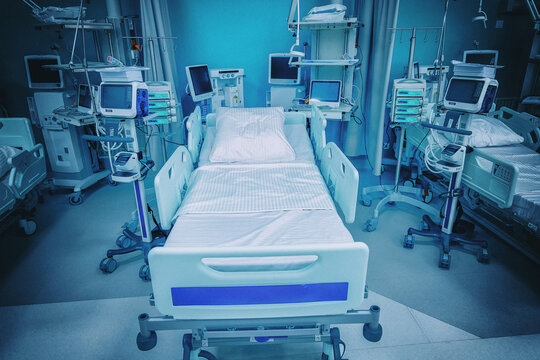 An empty bed stands in the middle of an intensive care unit of a new hospital. The photo is color graded in cold cyan tones with added film grain and a soft vignette. Cinematic medical mood